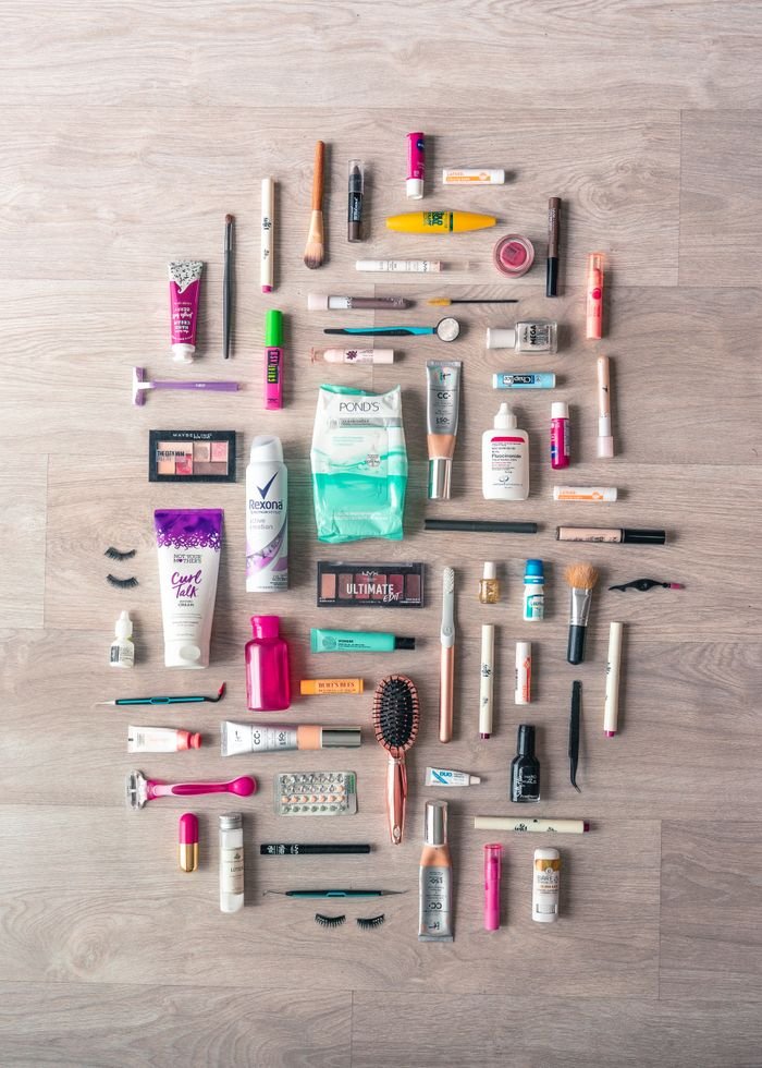 A diverse collection of beauty and grooming products neatly arranged on a wooden surface in a flatlay style.