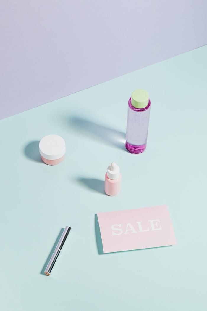 Flat lay of beauty and skincare products with a sale card on a pastel background.